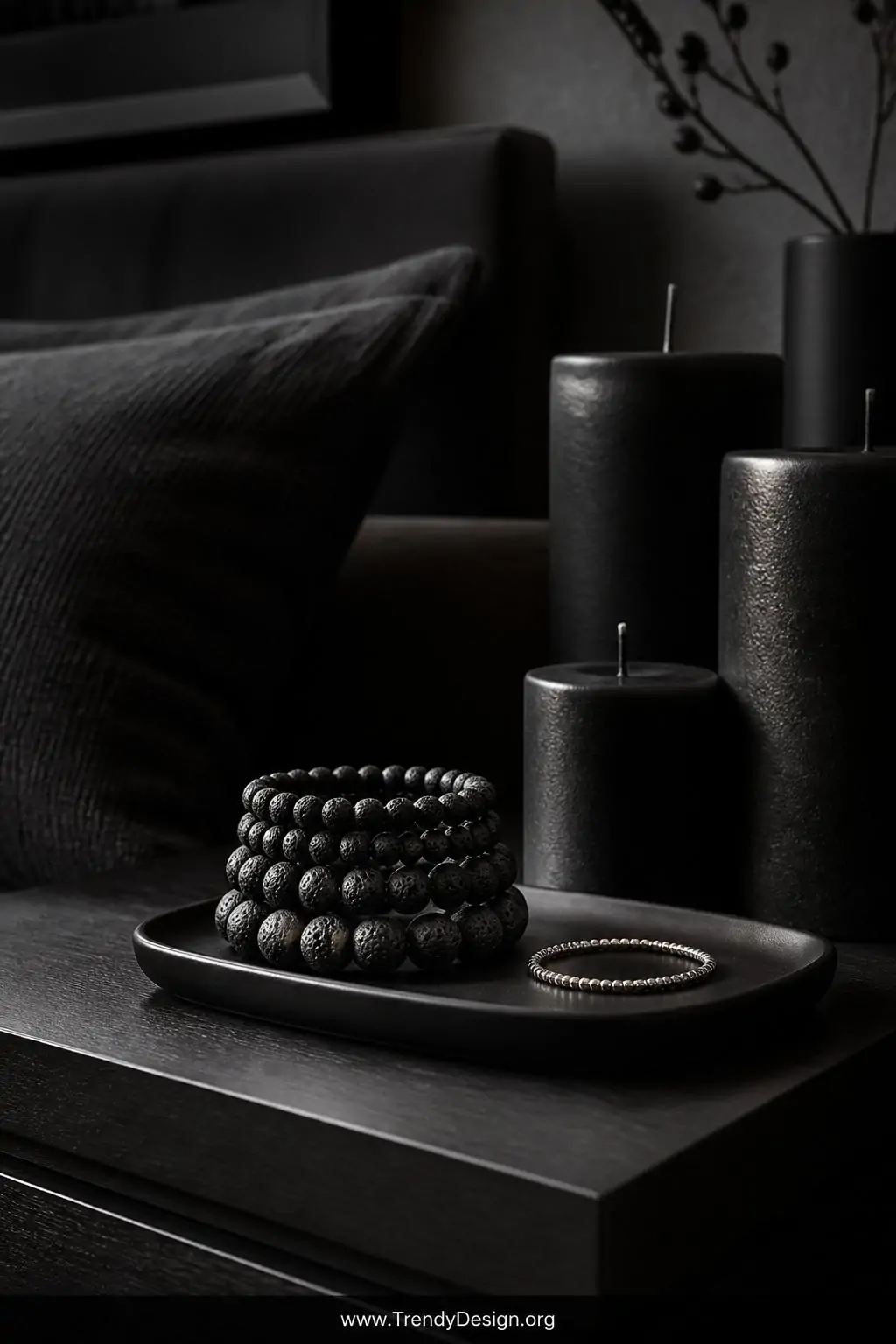 Wide shot of a minimalist dark bedroom vignette featuring a matte black ceramic tray holding a stack of graduated all-black l