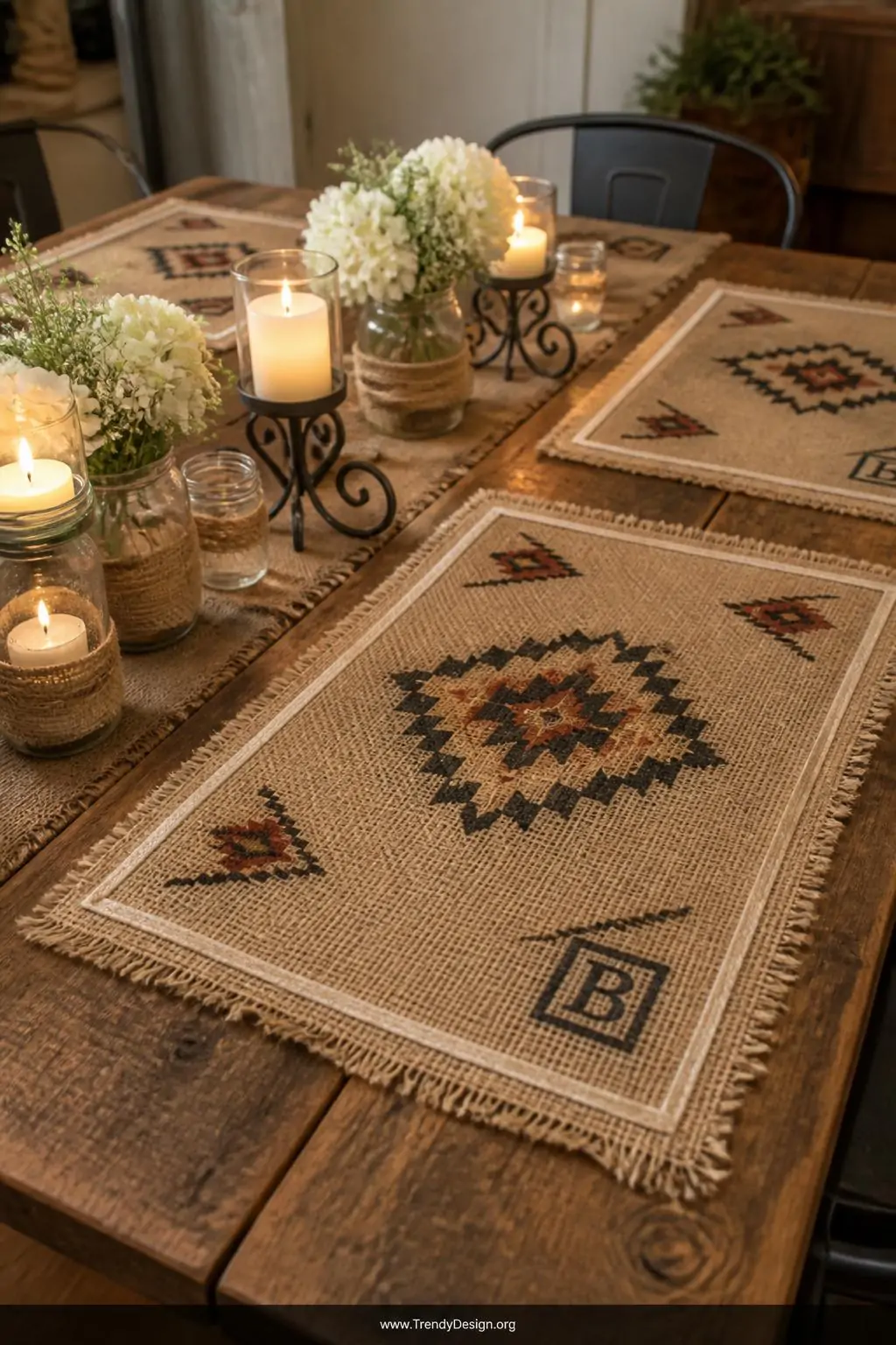 Medium shot of a weathered oak dining table set with stamped burlap placemats featuring geometric black and terracotta fabric
