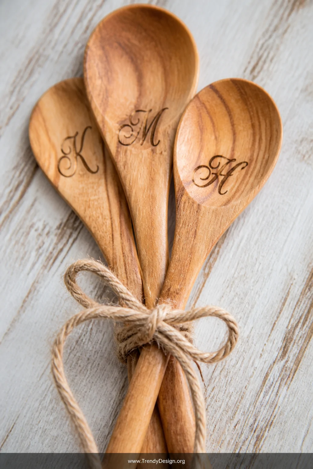 A close-up detail shot of three wooden spoons laid flat on a weathered white oak surface, each handle displaying elegantly bu
