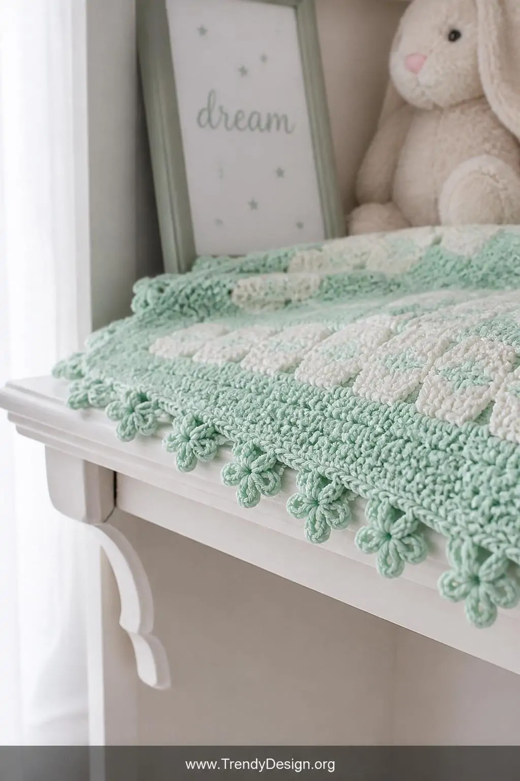 A close-up photorealistic shot of a delicate pastel mint C2C baby blanket edge resting on a white-painted wooden nursery shel