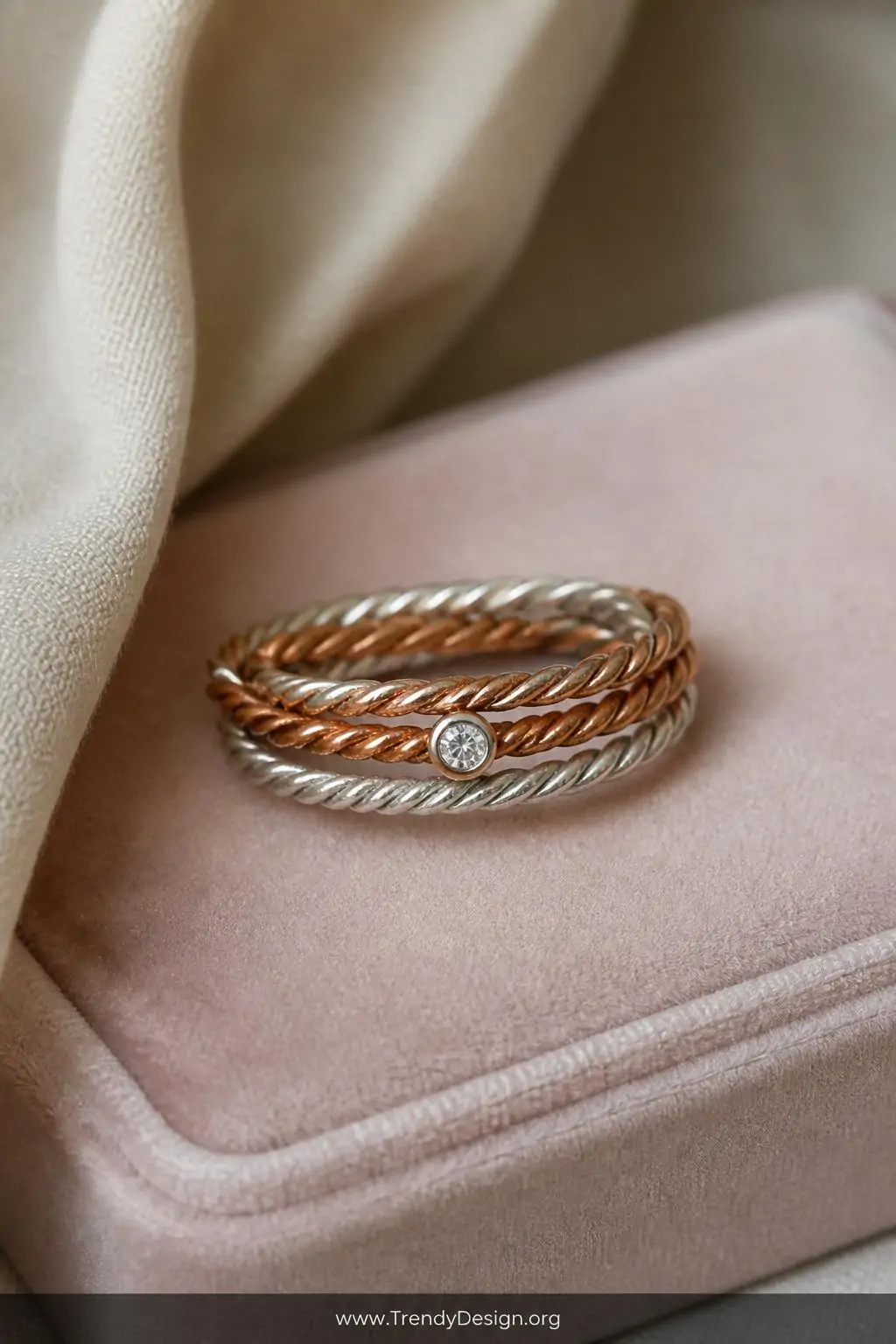 A close-up shot of a twisted two-tone copper and silver rope-textured band ring with a small faceted crystal accent at its ce