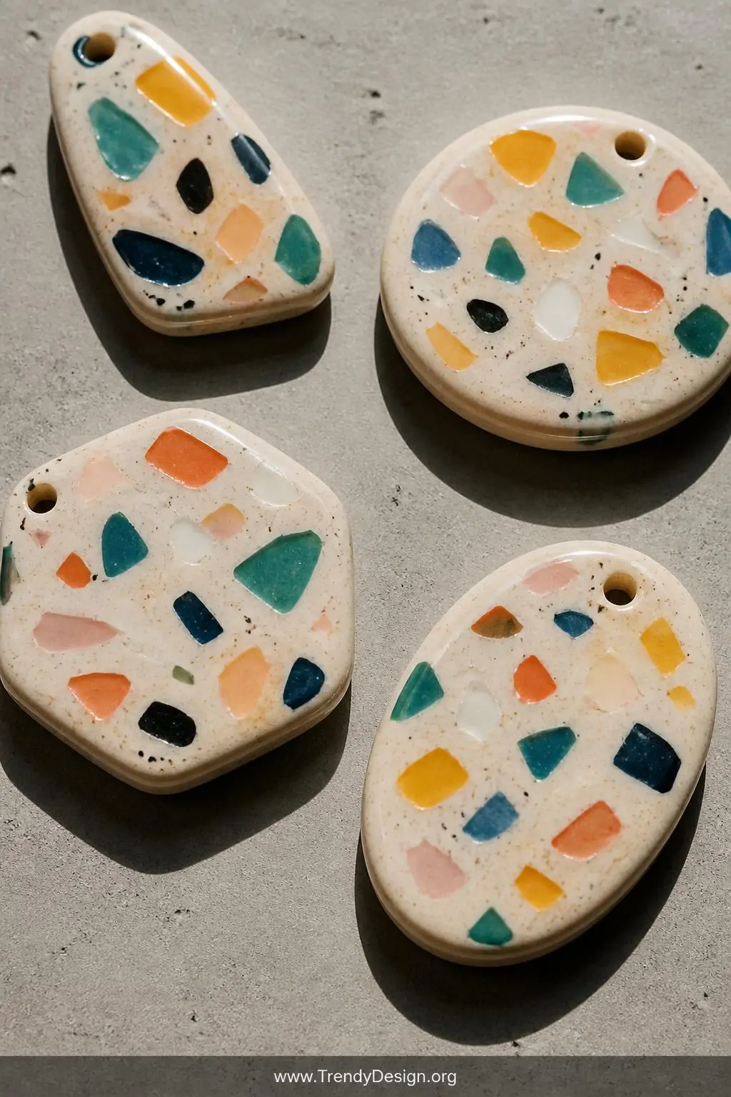 A closeup shot of terrazzo-style polymer clay pendants resting on a smooth concrete surface, each piece showing chaotic color