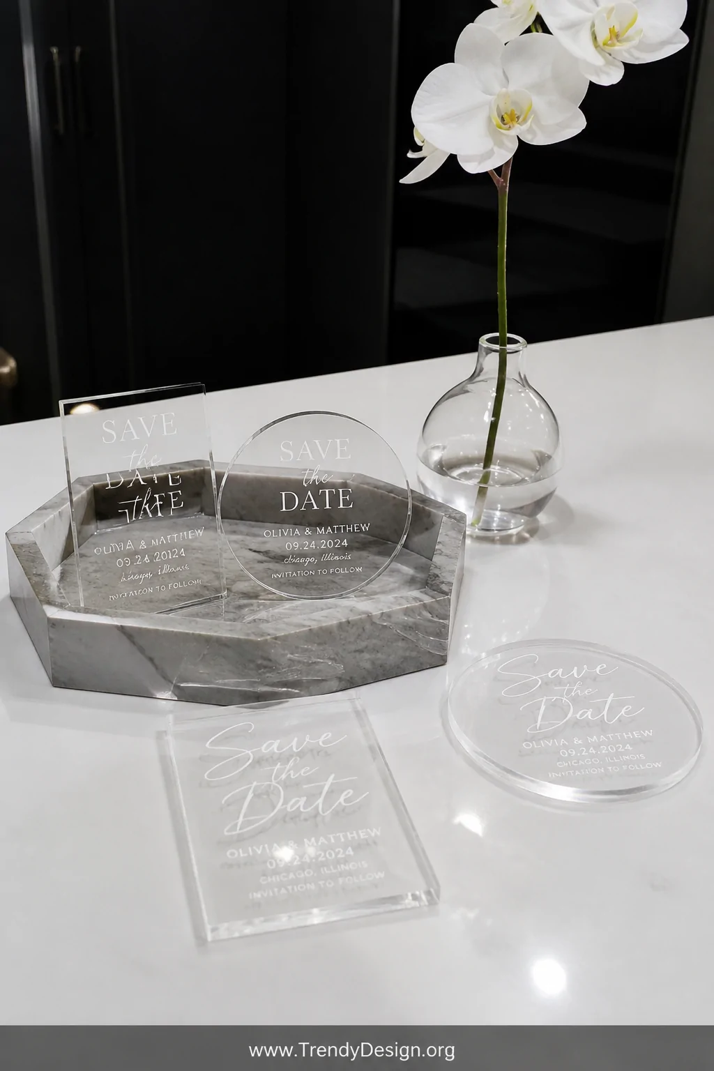 A wide styled vignette on a sleek white quartz surface displays a collection of small transparent acrylic rectangle and circl