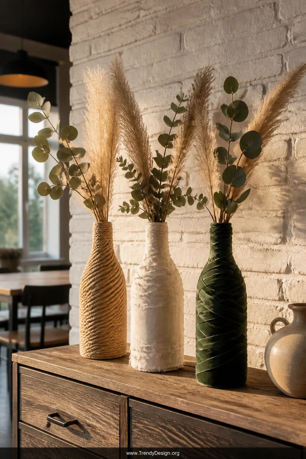 A medium shot of a rustic-modern dining room sideboard styled with three fabric-wrapped vessels converted from wine bottles a