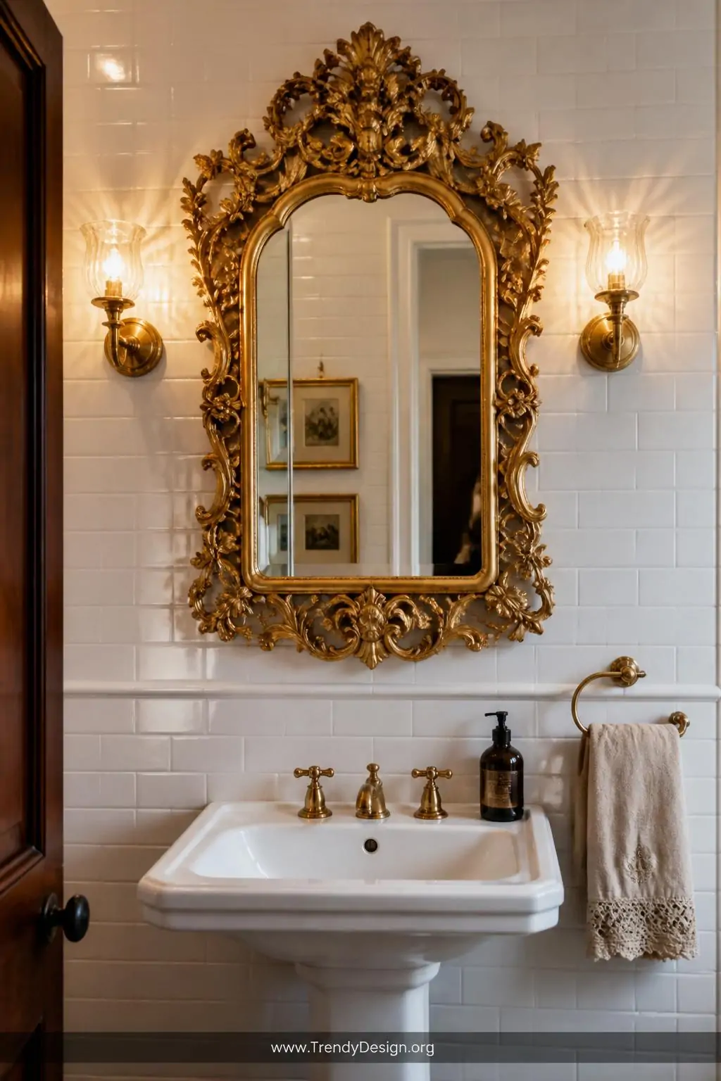 A heavily carved ornate gilded gold vintage mirror mounted dramatically against crisp white subway tiles above a classic pede