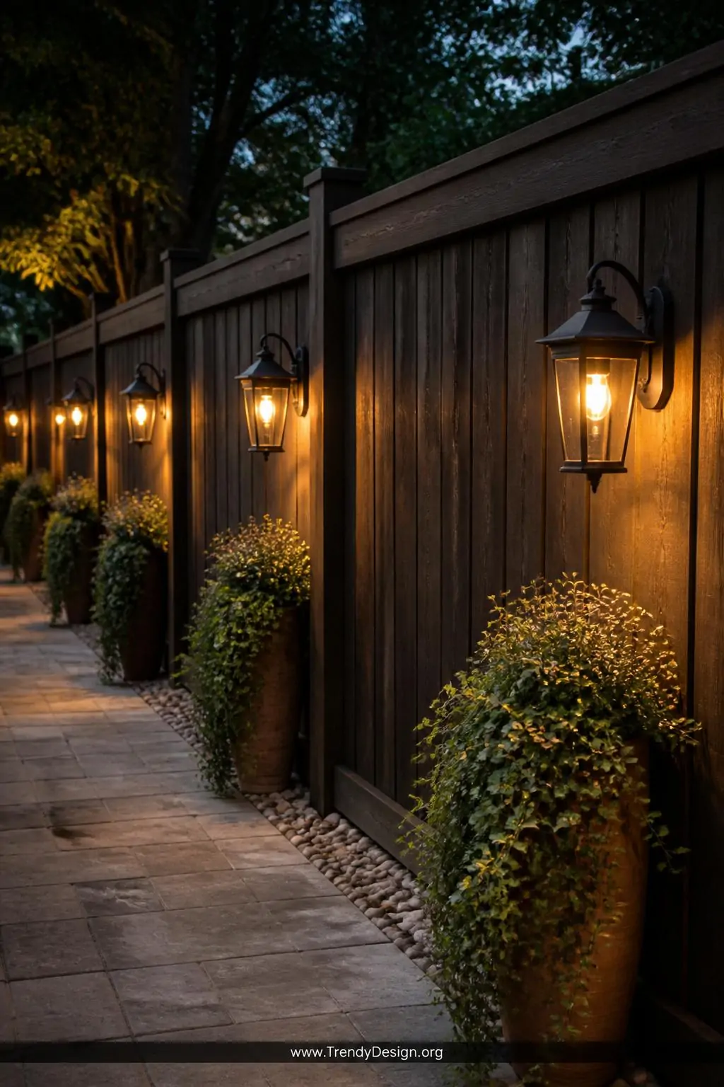 Medium shot of a long dark stained wooden privacy fence with evenly mounted black cast iron farmhouse lanterns casting warm a