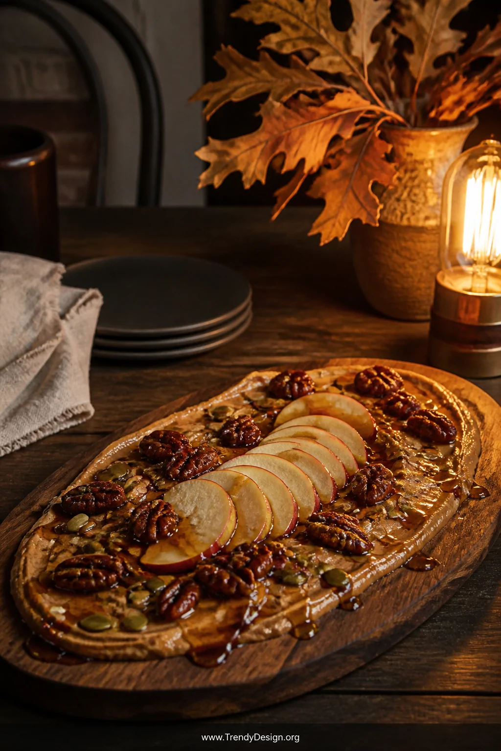 A medium-shot warm autumn vignette on a dark walnut farmhouse table, featuring a thick oval wooden board spread with cinnamon