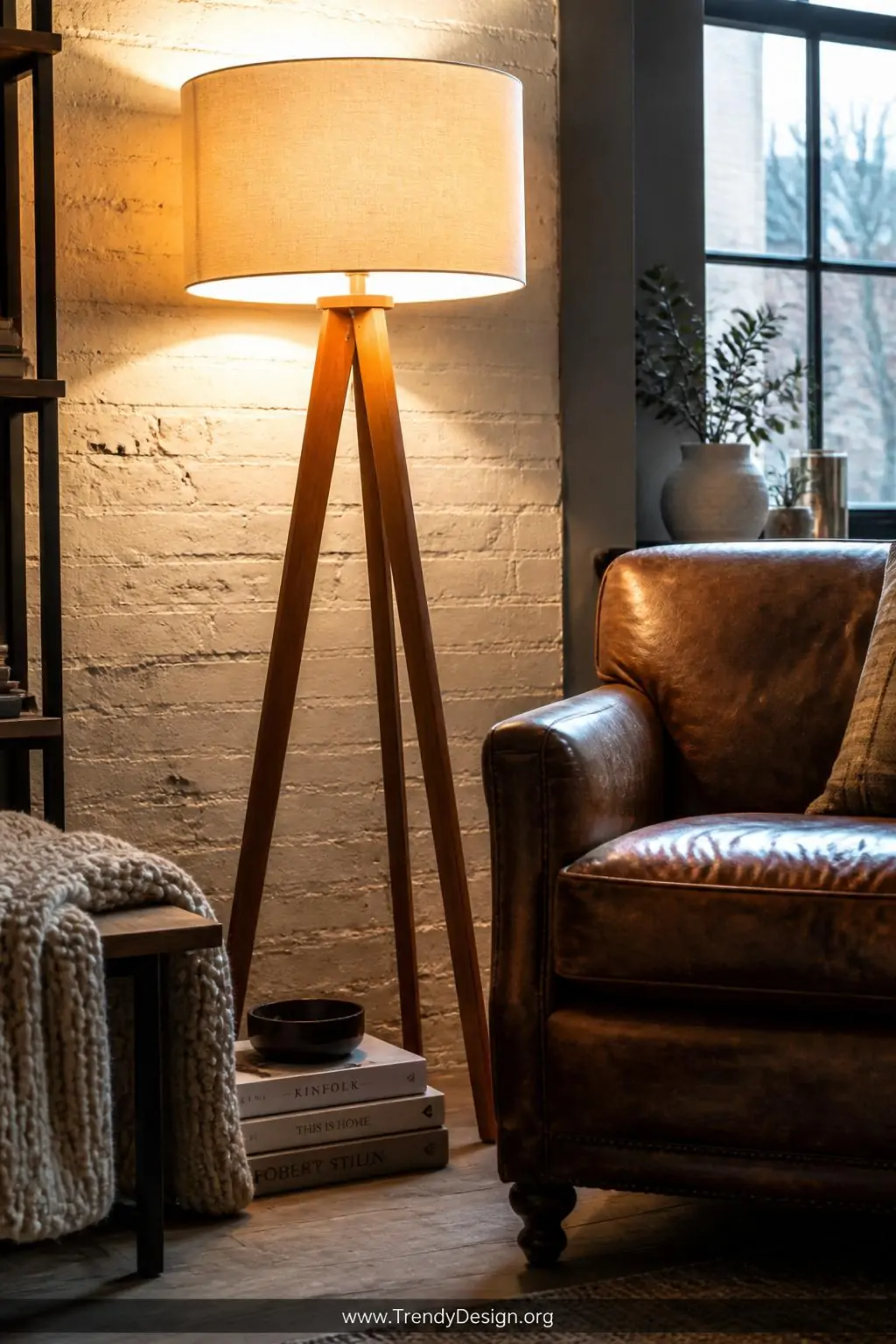 A Scandinavian tripod floor lamp with warm honey-toned wooden legs and a wide cream drum shade occupies a cozy reading corner