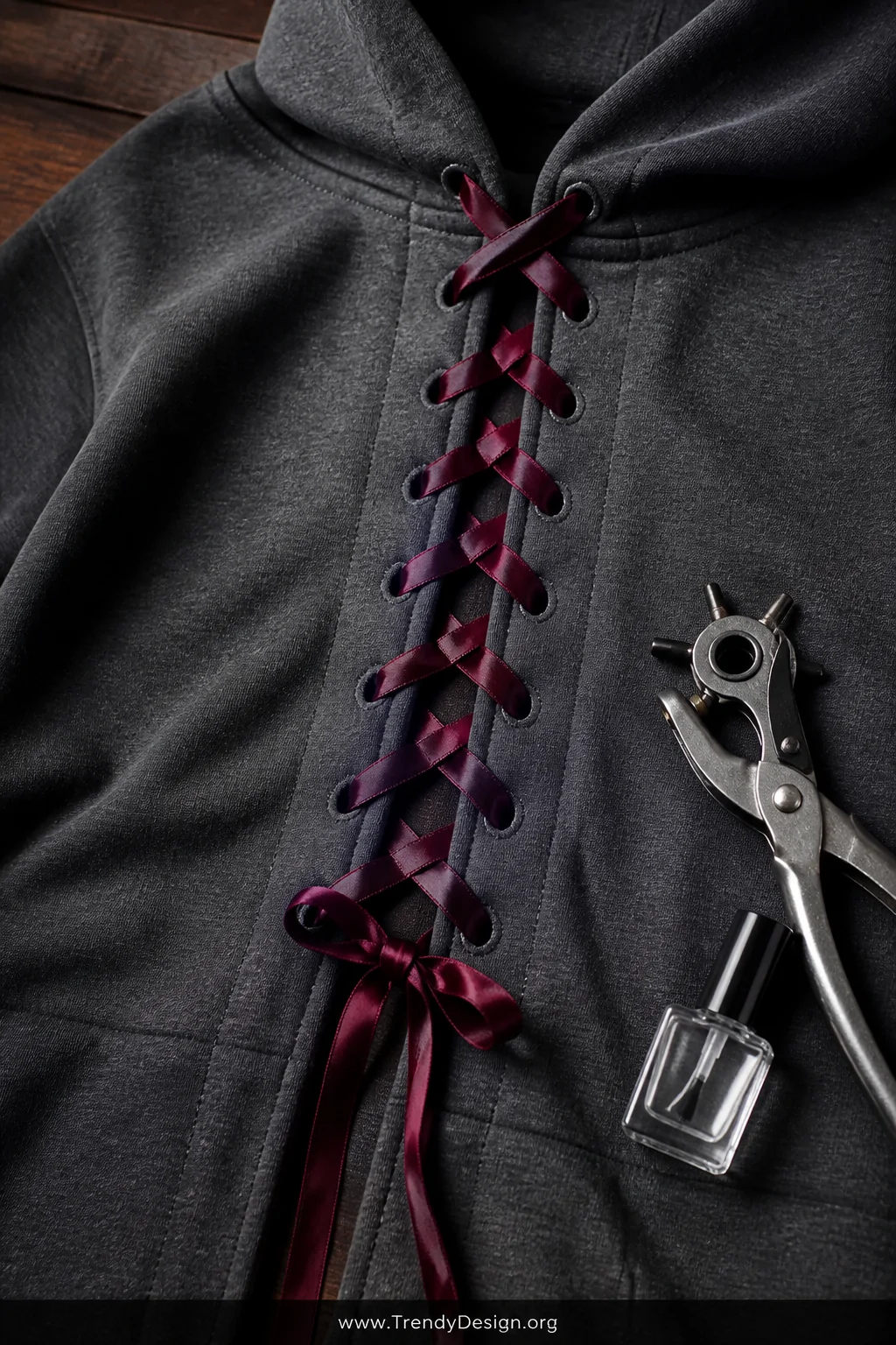 A detail closeup shot of a charcoal grey hoodie laid flat on a dark walnut wood surface, a vertical front slit laced with bur