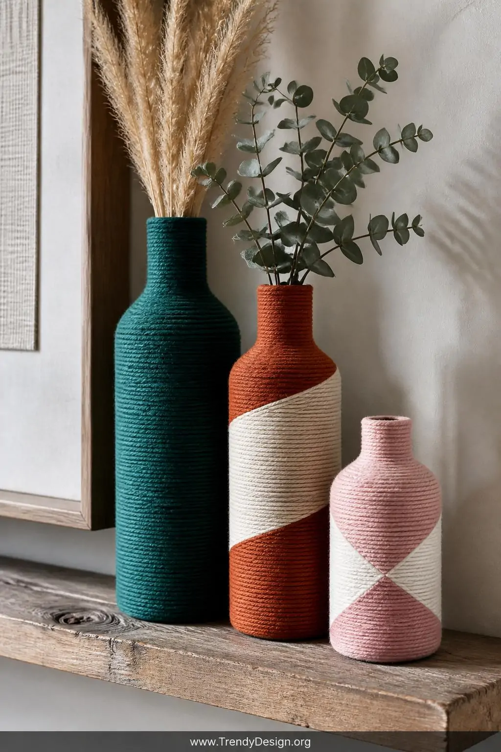 Closeup shot of three embroidery floss-wrapped glass bottles grouped on a reclaimed wood shelf, the tallest bottle fully wrap