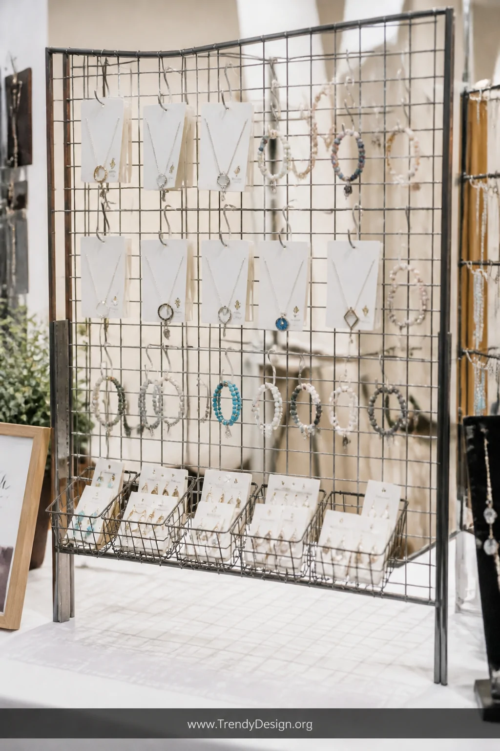 Medium shot of a freestanding wire grid panel display at a craft show booth, multiple silver S-hooks suspending necklace card