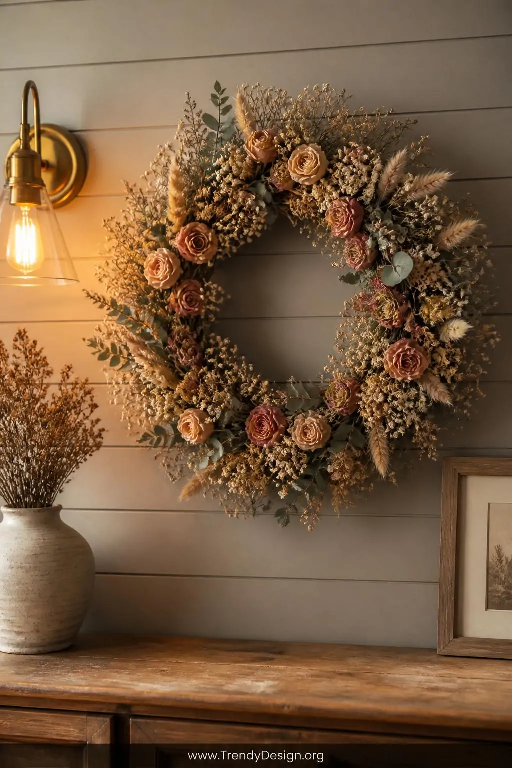 A medium shot of a rustic gallery wall featuring a lush circular dried flower wreath centered against warm greige painted shi