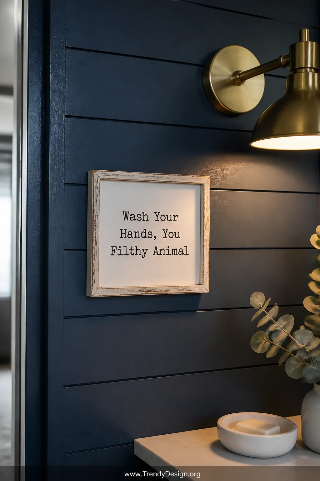 Close-up detail shot of a moody bathroom wall featuring deep navy painted shiplap, a small distressed white framed sign readi