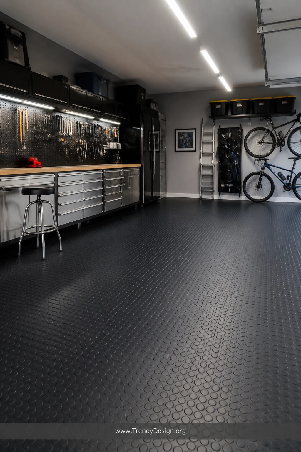 Medium wide shot of a clean organized garage interior with charcoal coin-pattern rubber tile flooring covering the entire con