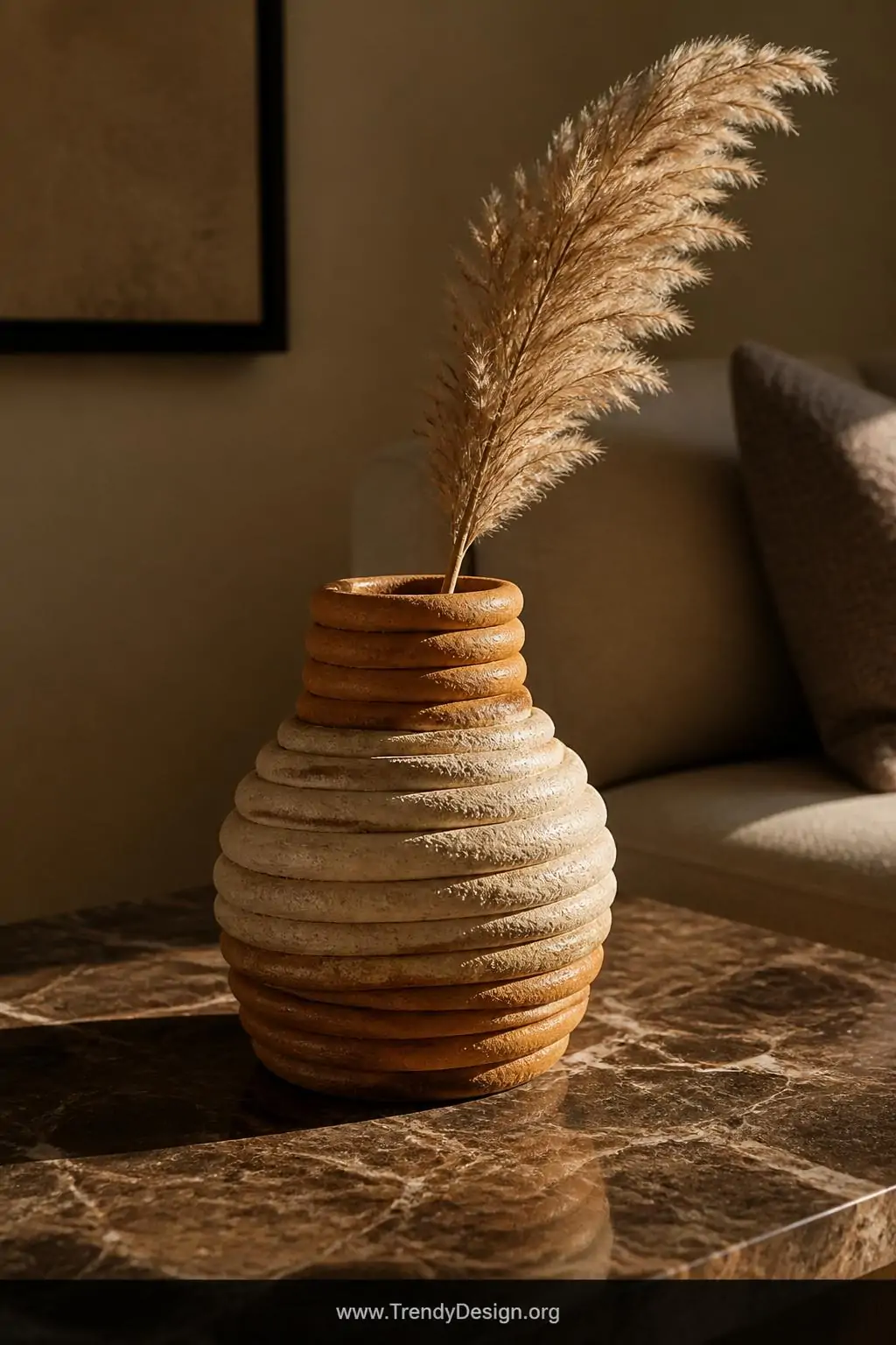 A closeup shot of a handbuilt coil vase sitting on a marble side table, its raw visible clay coils stacked in earthy ochre an