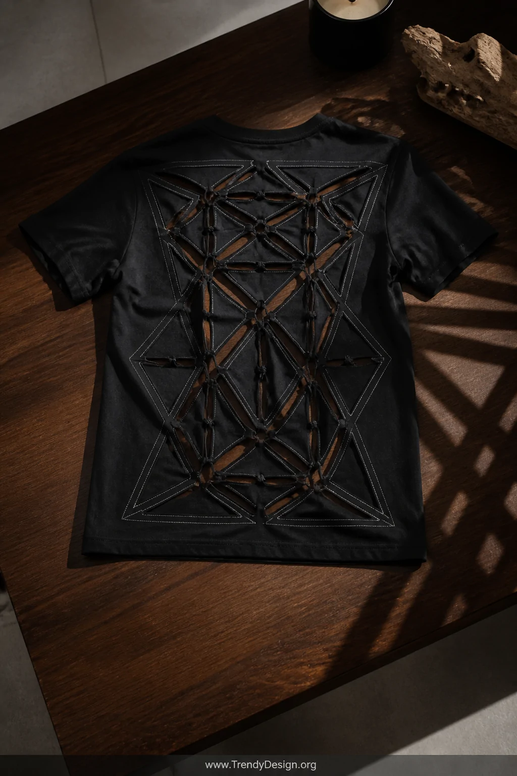 A wide shot of a black t-shirt laid back-panel-up across a dark walnut table under sharp overhead studio lighting, the entire