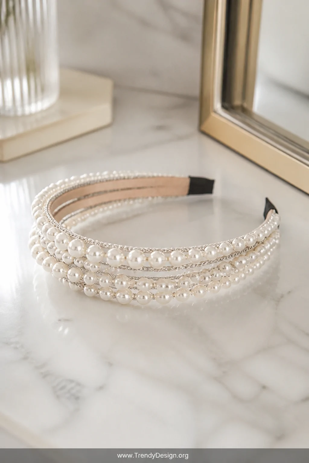 A closeup detail shot of a delicate headband wrapped in layered faux pearl strands and thin silver chain resting on a marble 