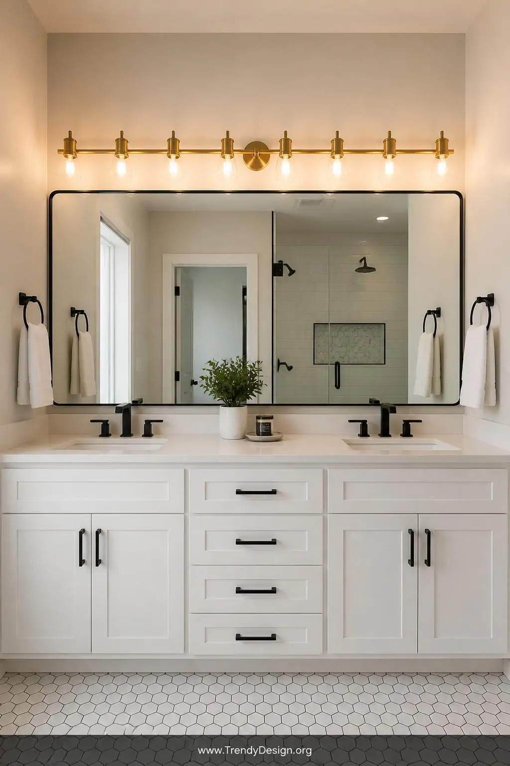 A wide-shot modern bathroom featuring a long multi-bulb exposed brass bar light spanning the full width above a double vanity