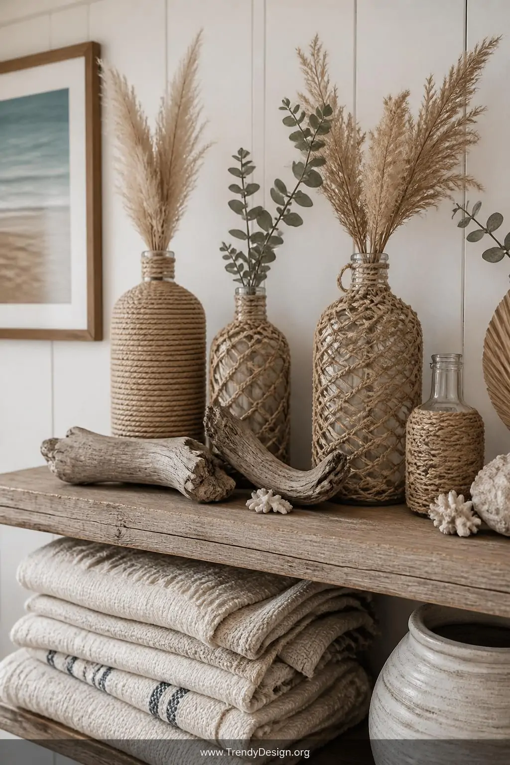 Medium shot of a relaxed coastal living room shelf styled with rope-wrapped jute and sisal glass bottles in natural sand tone