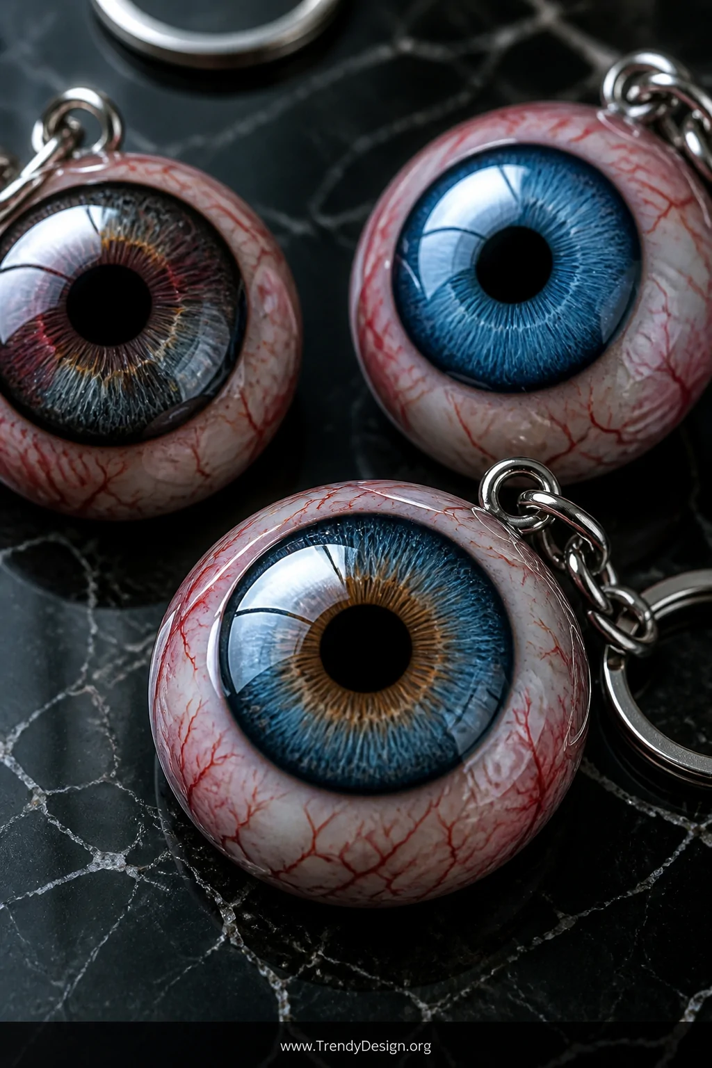 Extreme closeup detail shot of three glossy resin eyeball keychains resting on a black marble surface, each featuring vivid p
