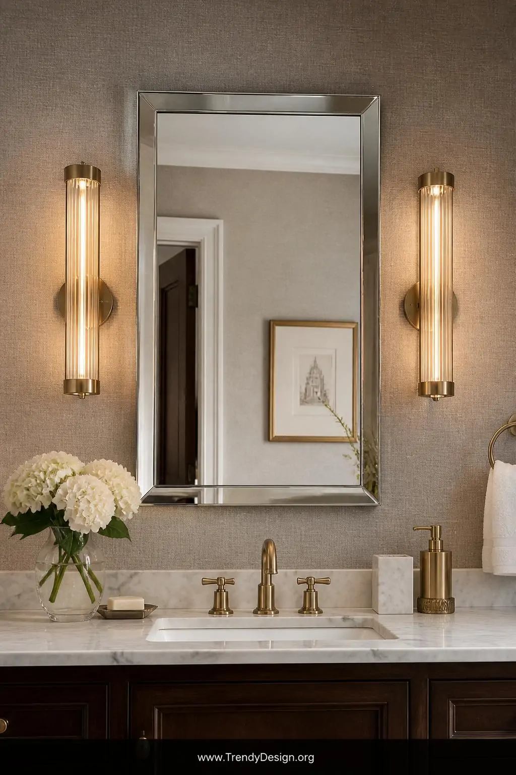 A medium-shot photorealistic bathroom wall vignette displaying two slim antique brass cylindrical sconces mounted symmetrical
