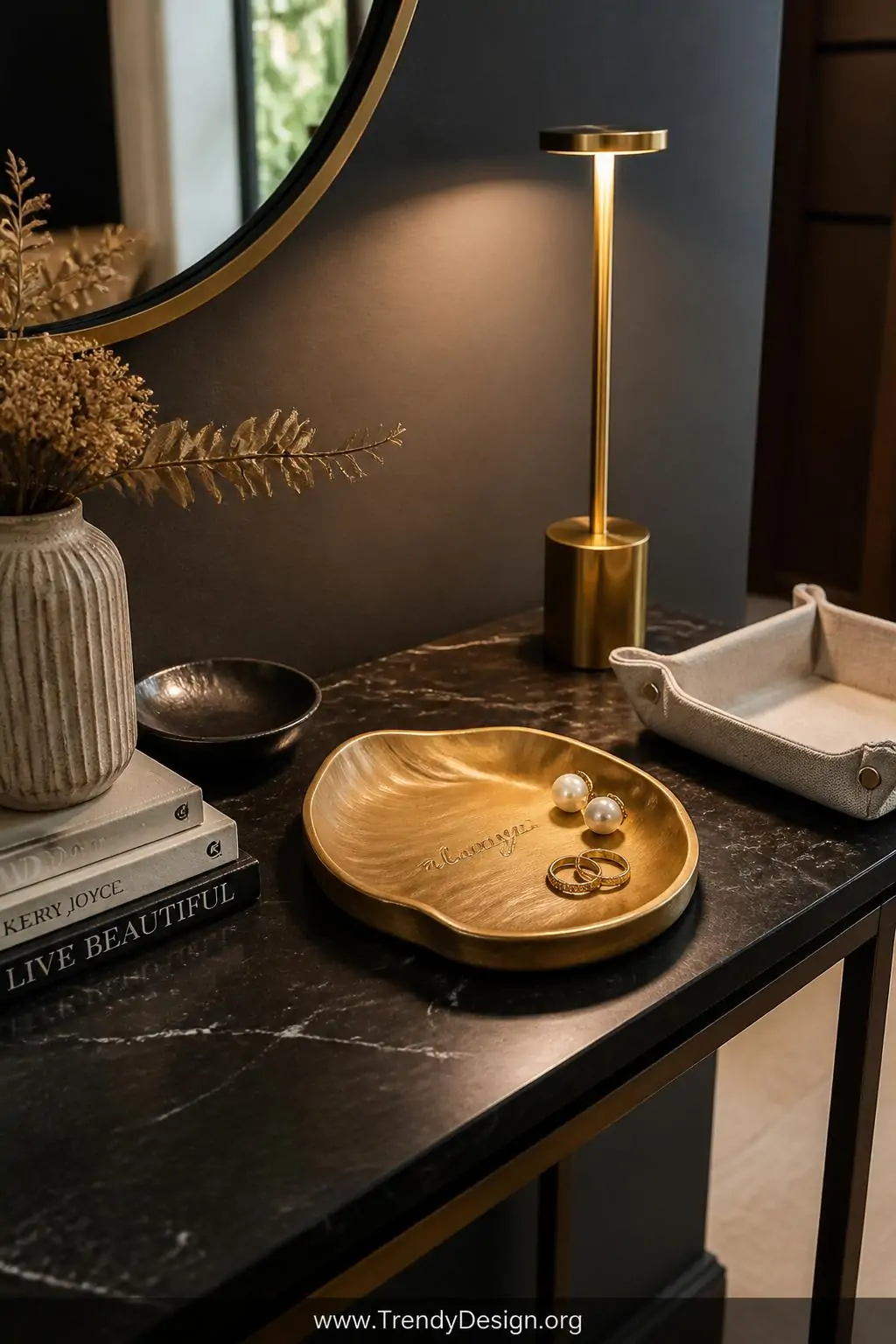 A medium shot of a styled entryway table displaying a small wavy-edged clay trinket dish painted in deep matte gold, holding 