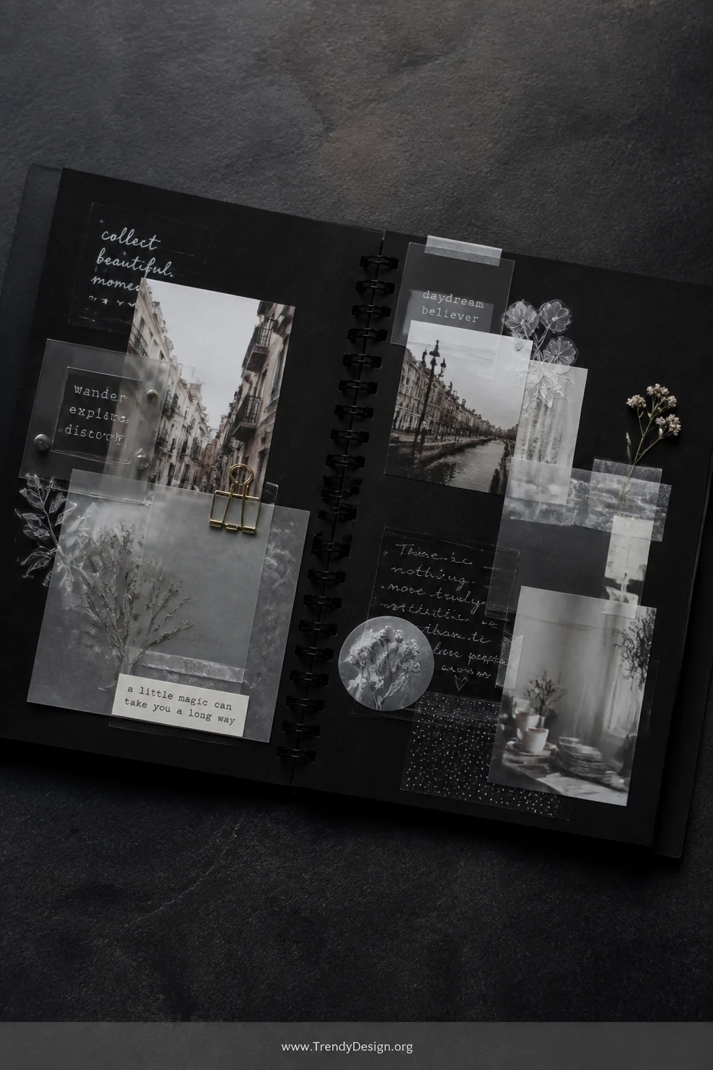A wide-shot photorealistic styled flat-lay of a black scrapbook spread on a dark slate surface under soft cool studio lightin