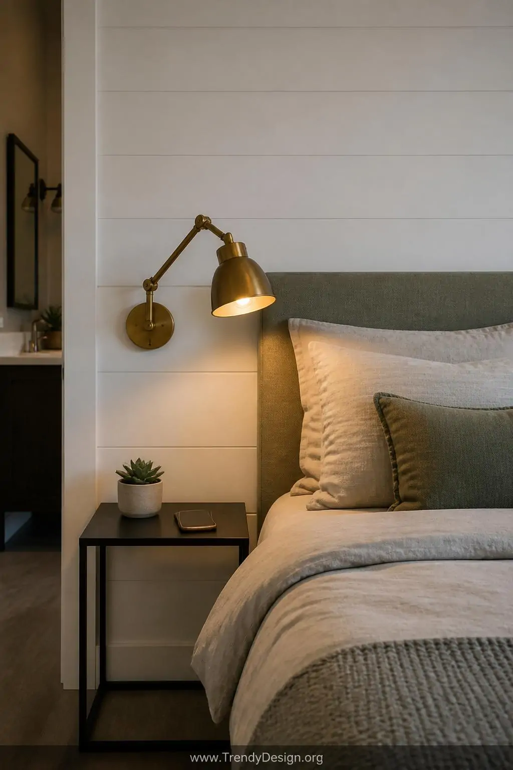 A medium wide shot showcases a minimalist bedroom wall where a polished brass swing-arm sconce is mounted at reading height b