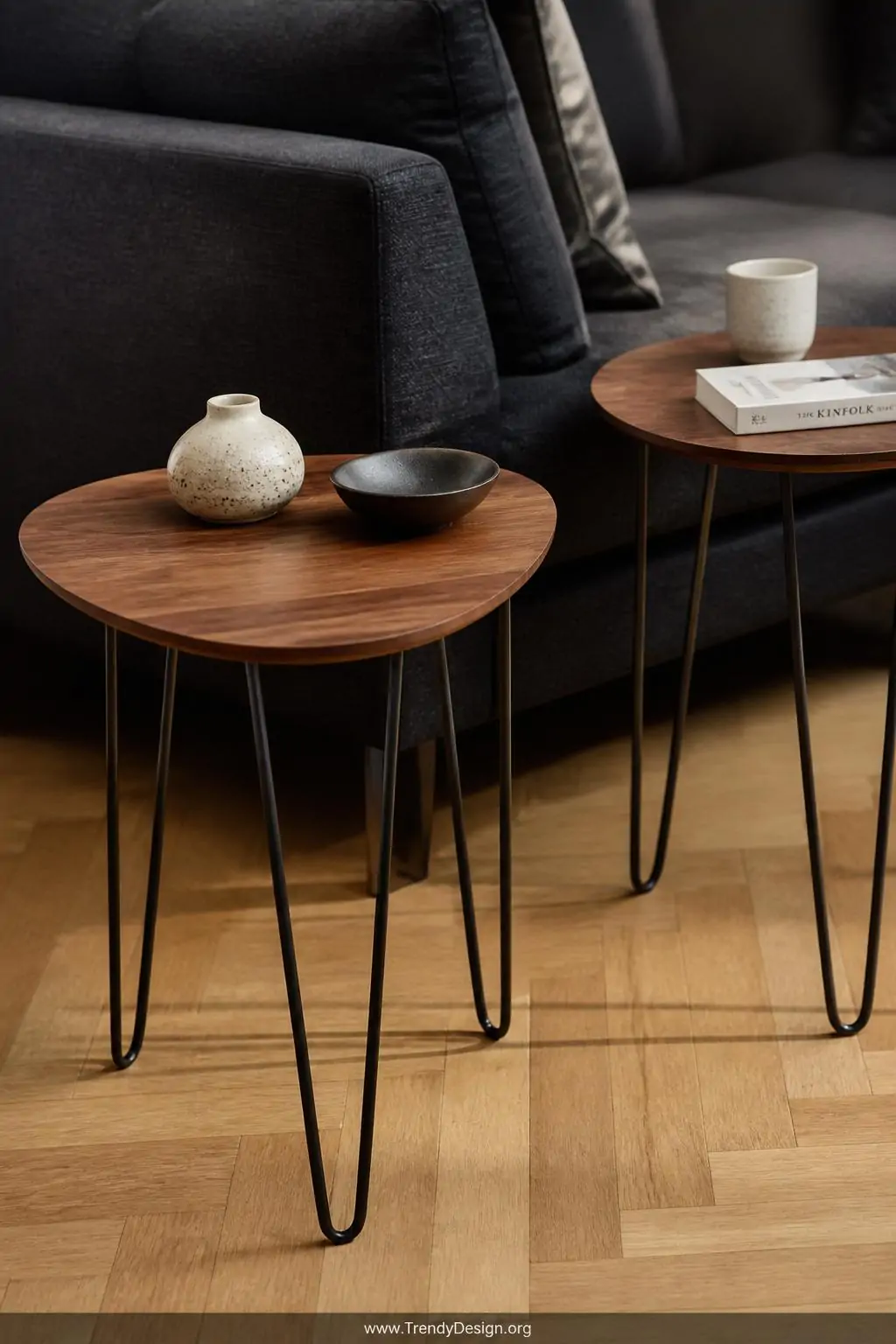 Two slender hairpin leg side tables with warm walnut tops flank a charcoal linen sofa, their thin bent-steel legs creating de