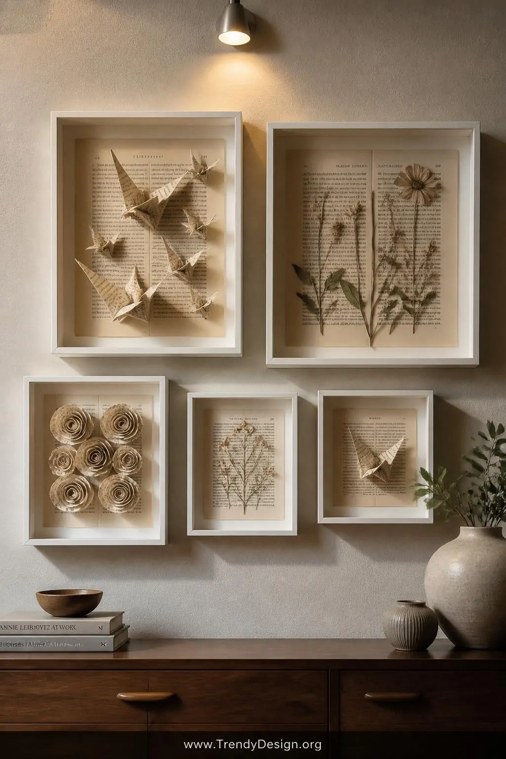 A styled gallery wall above a mid-century console table featuring framed repurposed book page art including intricately folde
