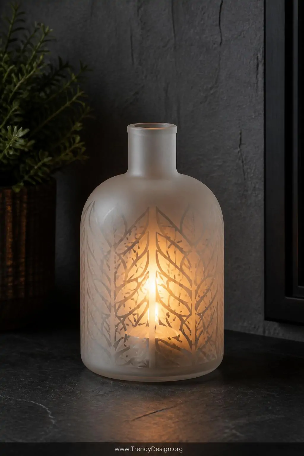 Closeup shot of a frosted etched glass bottle candle holder on a dark slate surface with a glowing tealight inside illuminati