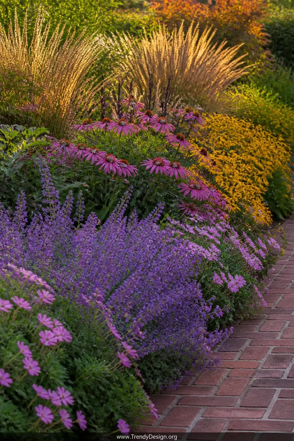 Medium shot of a layered perennial flower border in late summer peak bloom, purple catmint and soft pink geraniums spilling a