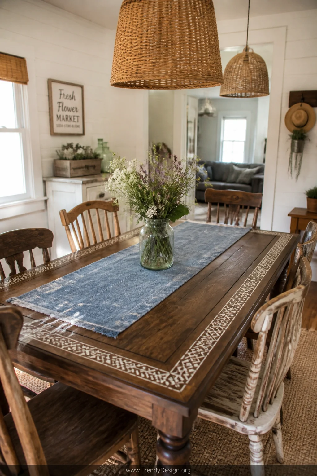 A wide room shot of a farmhouse dining table refinished in a rich warm walnut stain with a crisp white stenciled geometric di