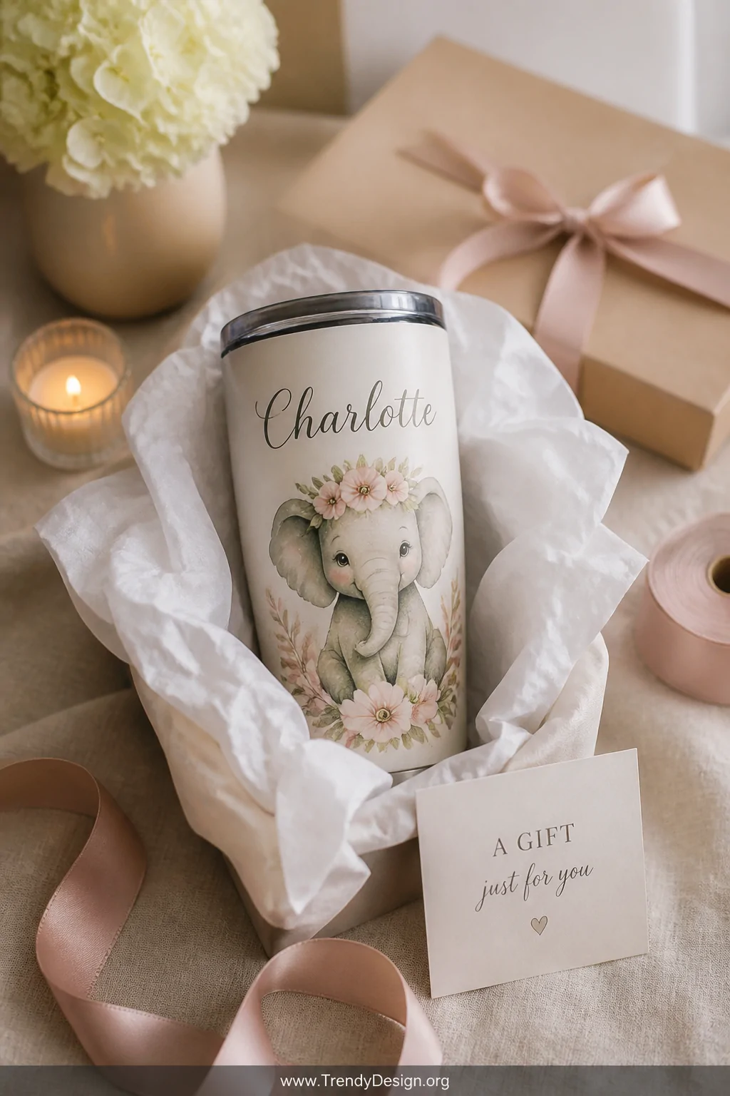 A medium shot of a gift-ready flat lay scene on a light linen surface featuring a personalized elephant tumbler with elegant 