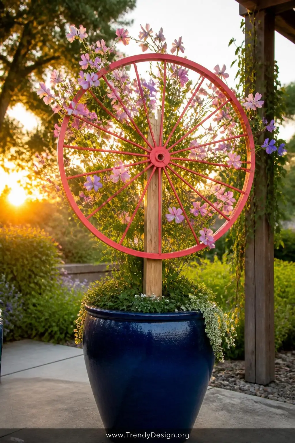 A wide shot of a statement garden vignette centered on an oversized glazed navy blue pot with a vintage bicycle wheel spray-p