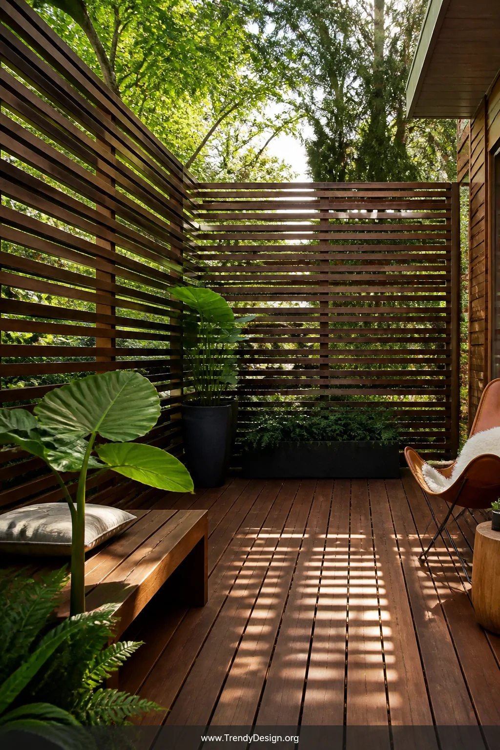 Medium shot of a ground-level deck enclosed by evenly spaced horizontal cedar slat privacy screens, warm honey and amber wood