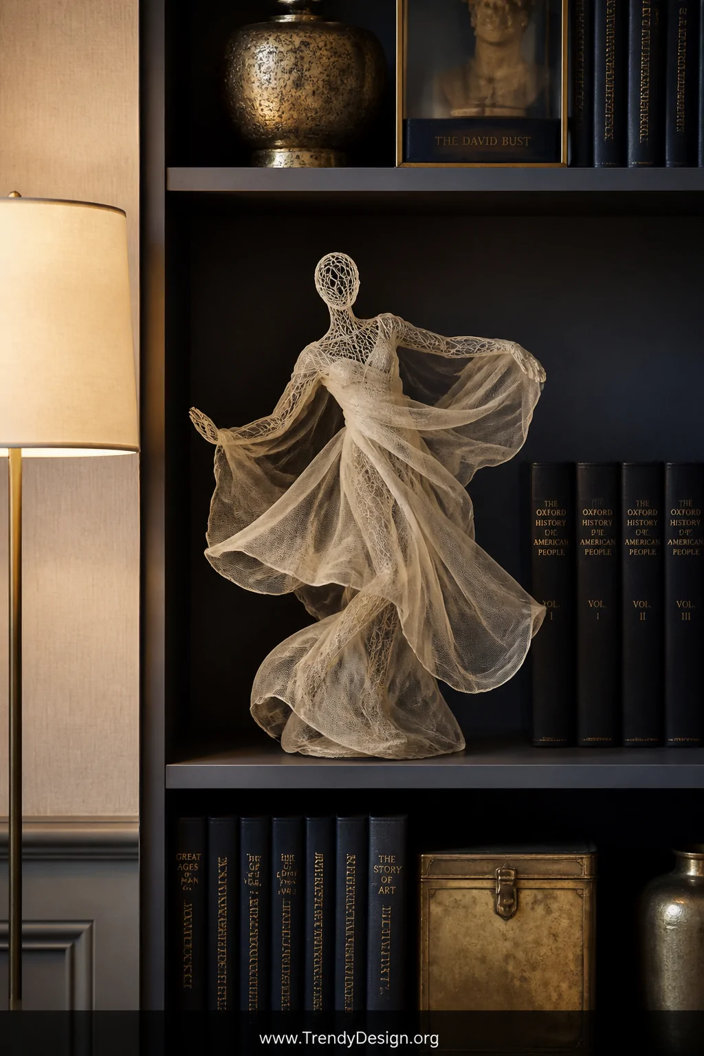 A styled bookshelf vignette in medium shot featuring a wire-framed fabric sculpture of an abstract dancing human figure posit
