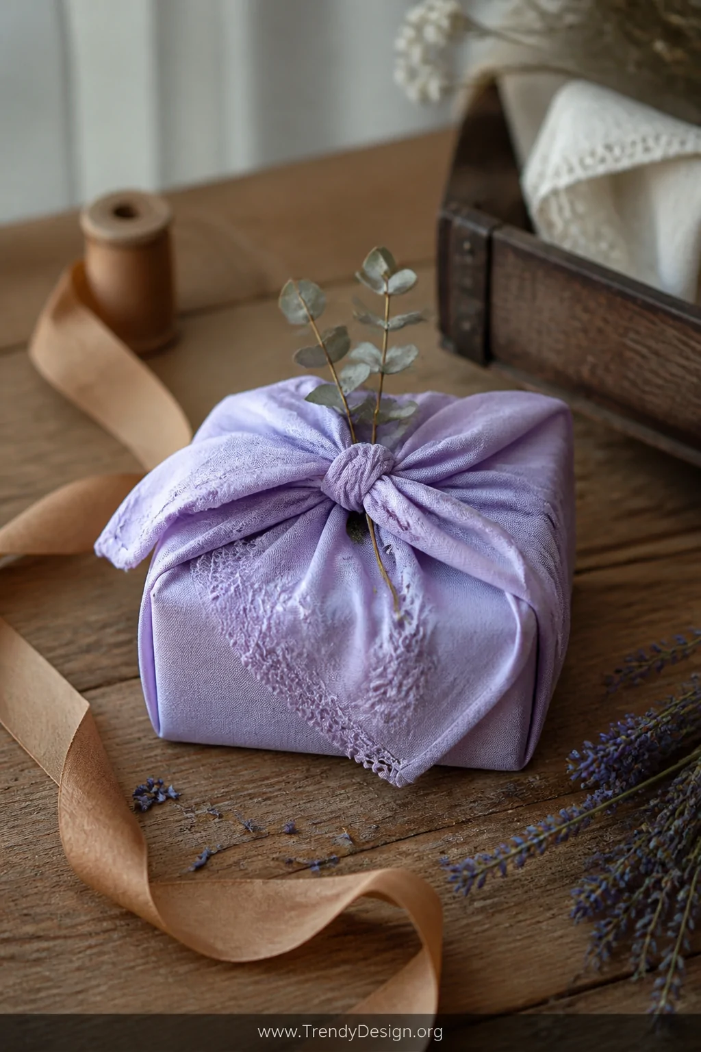 A rustic wooden tabletop medium shot featuring a small gift box wrapped in a pale lavender embroidered vintage handkerchief, 
