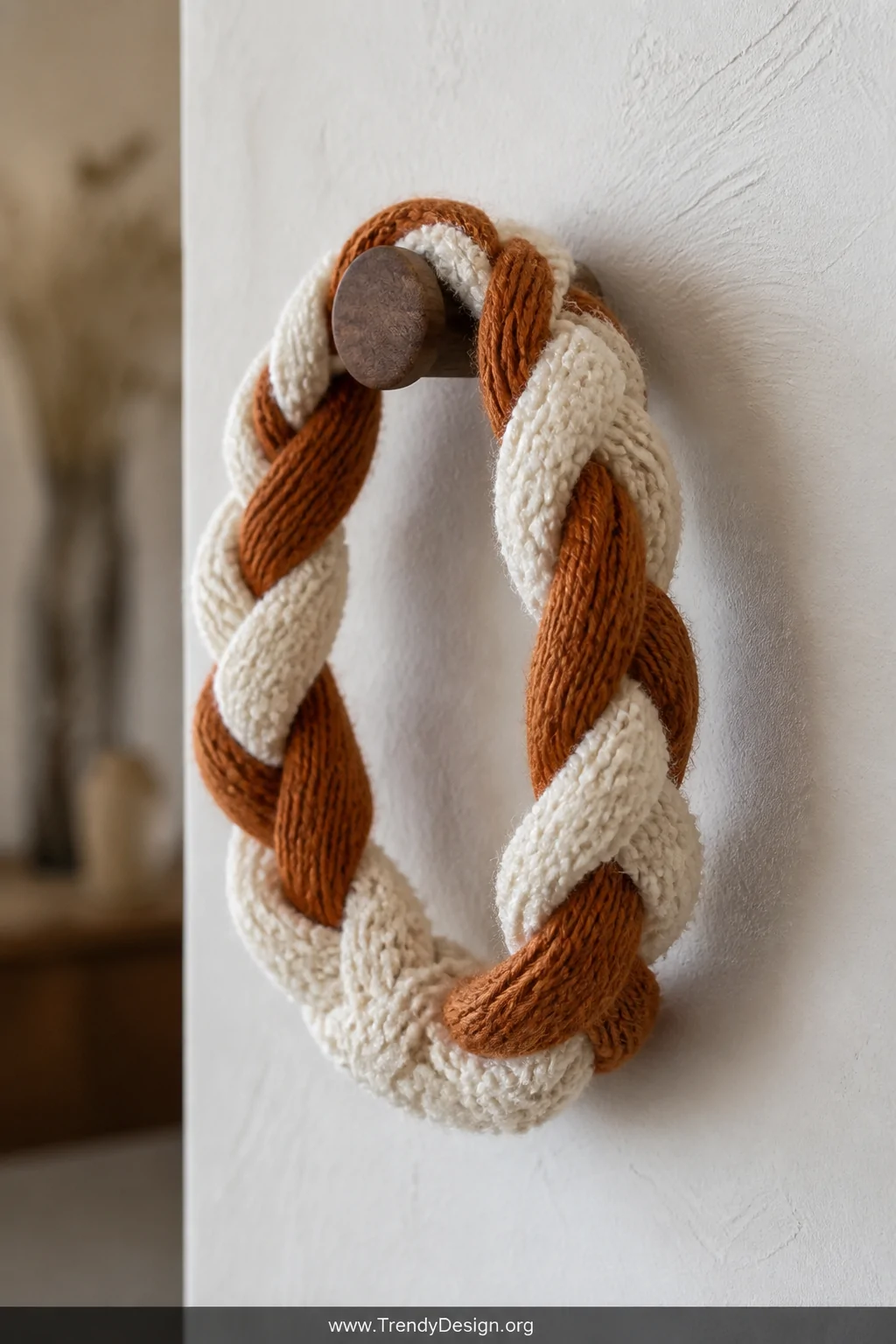 A closeup detail shot of a thick braided headband combining chunky ivory bouclé yarn and smooth rust-colored worsted weight y