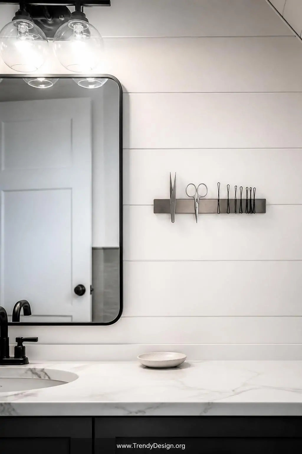 Medium shot of a sleek magnetic metal strip mounted on a white shiplap wall beside a bathroom mirror, holding silver tweezers