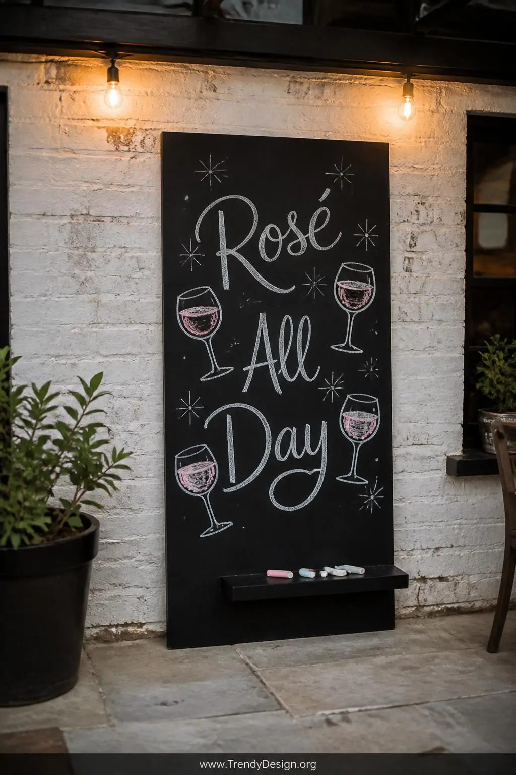 A cooler with a single matte black chalkboard-painted panel propped against a whitewashed brick outdoor wall, 