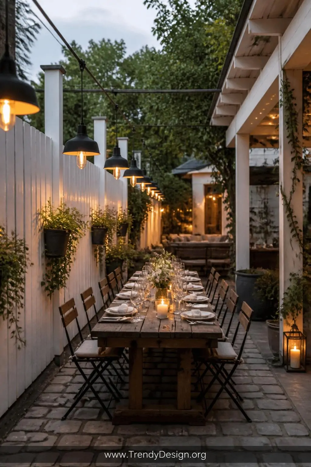 Wide shot of an outdoor dining area between a white painted fence and a pergola structure, matching matte black pendant light
