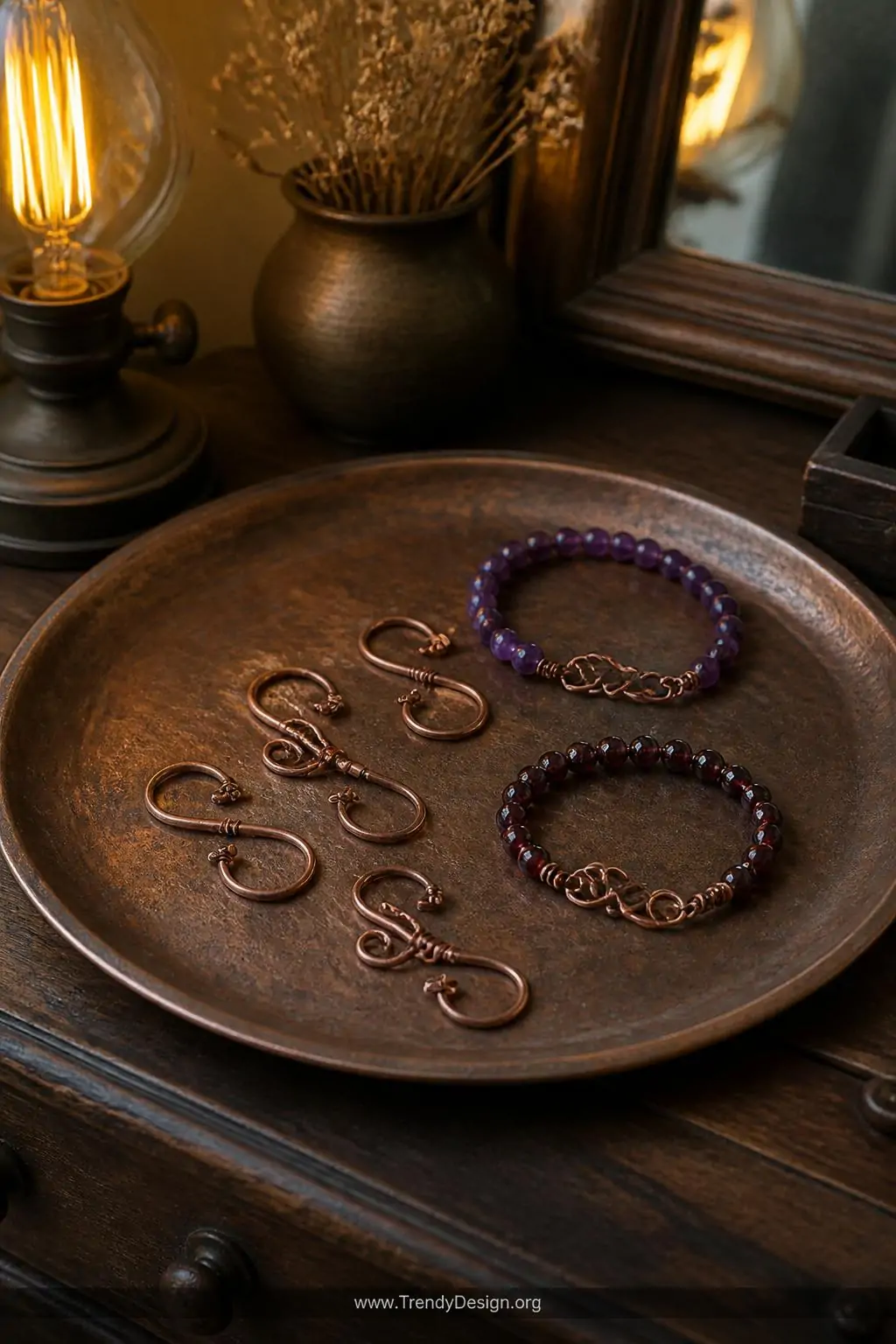 A weathered copper tray atop a dark walnut dresser displays handcrafted wire S-hook closures alongside amethyst and garnet be