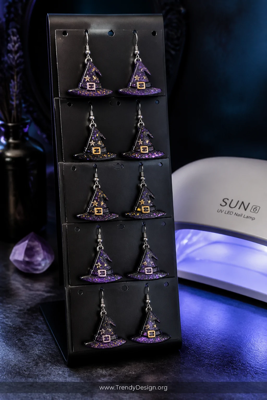 Medium closeup of five pairs of purple and black holographic glitter resin witch hat earrings displayed on a matte black jewe