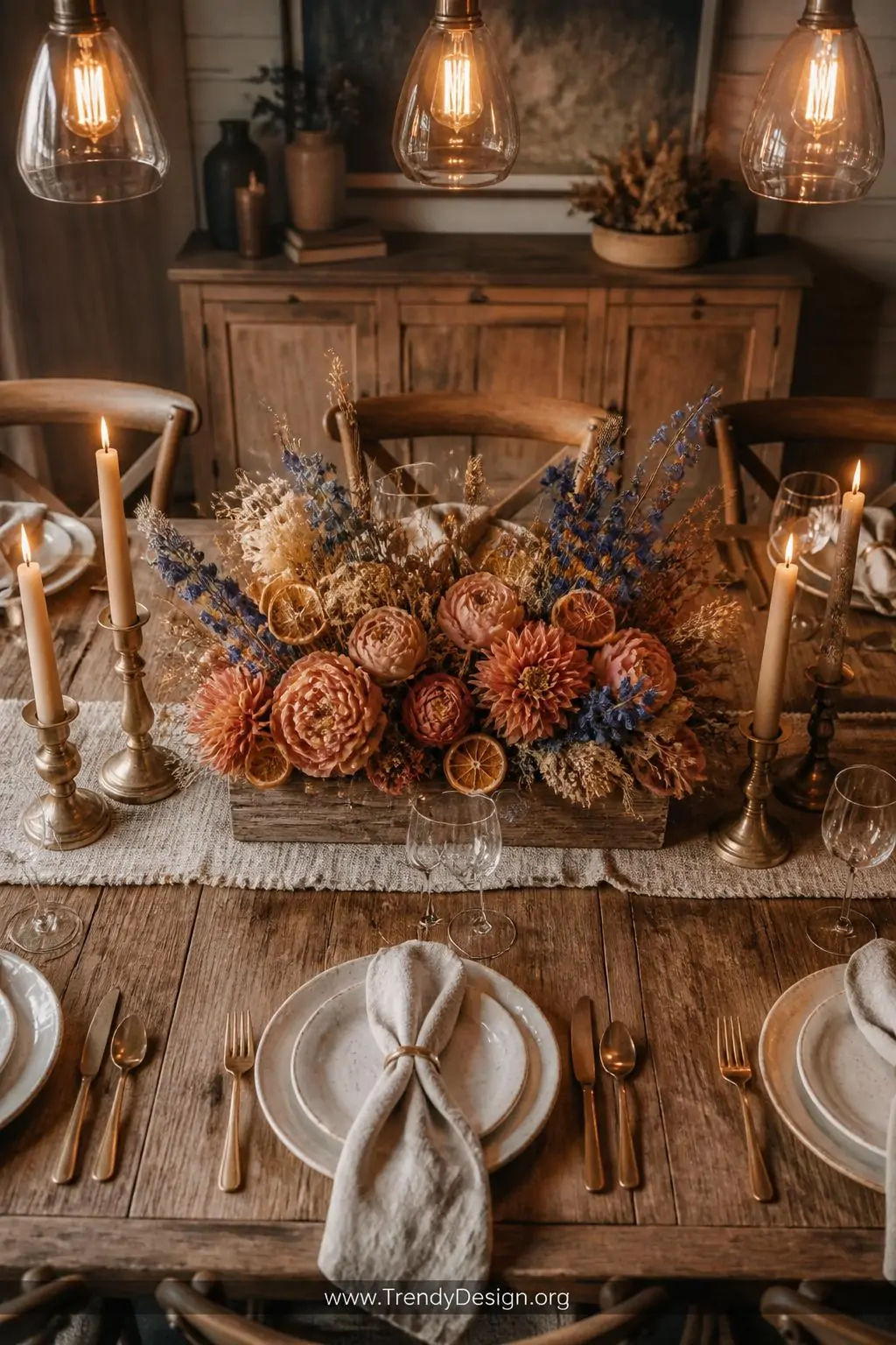 A medium overhead shot of a farmhouse dining table set with linen napkins and aged brass candlesticks, centered with a low re
