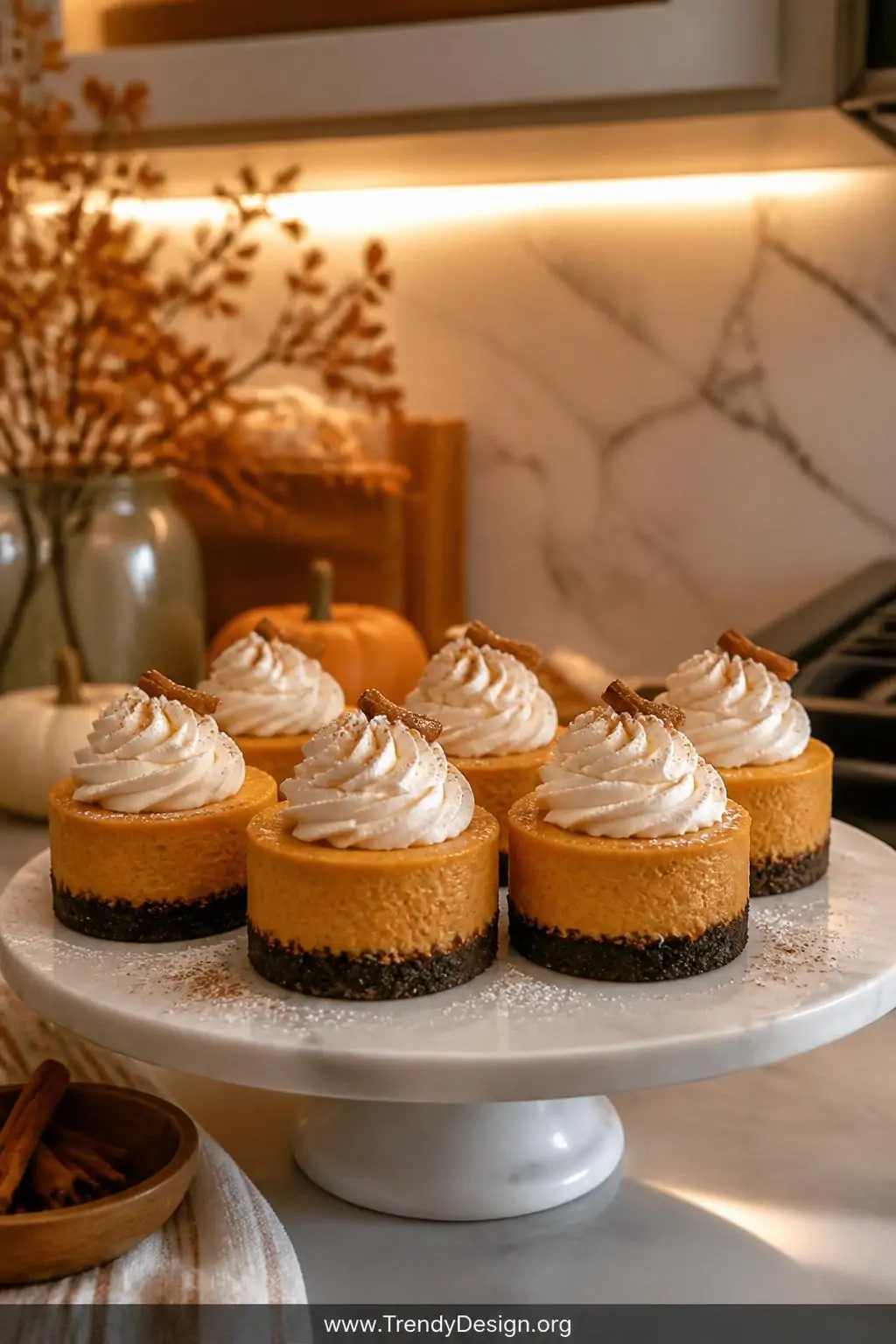 A close-up shot of a marble cake stand on a cozy styled kitchen counter, presenting perfectly portioned mini pumpkin cheeseca