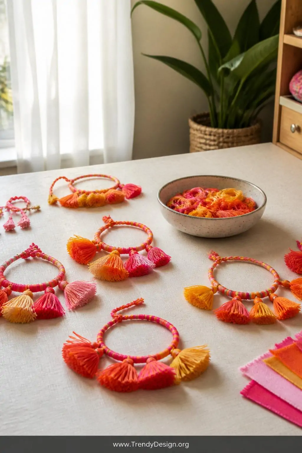 Medium shot of a bright craft room tabletop scattered with hot pink, orange, and yellow embroidery floss tassel bracelets arr
