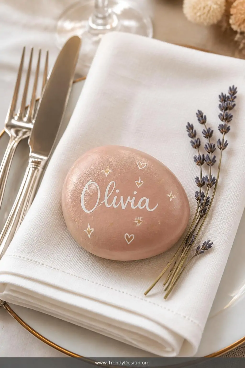 Close-up shot of a beautifully styled table place setting featuring a smooth flat river rock painted in a solid matte blush b