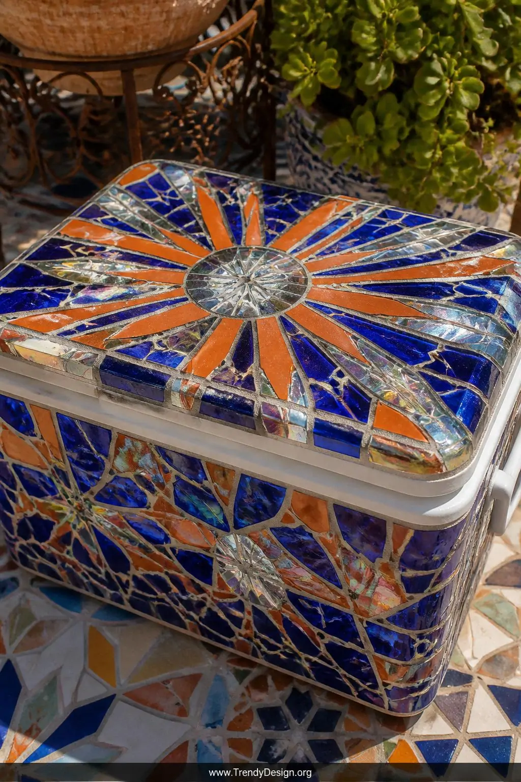 A cooler encrusted in a vivid mosaic of cobalt blue sea glass, terracotta broken tile shards, and iridescent mirror fragments