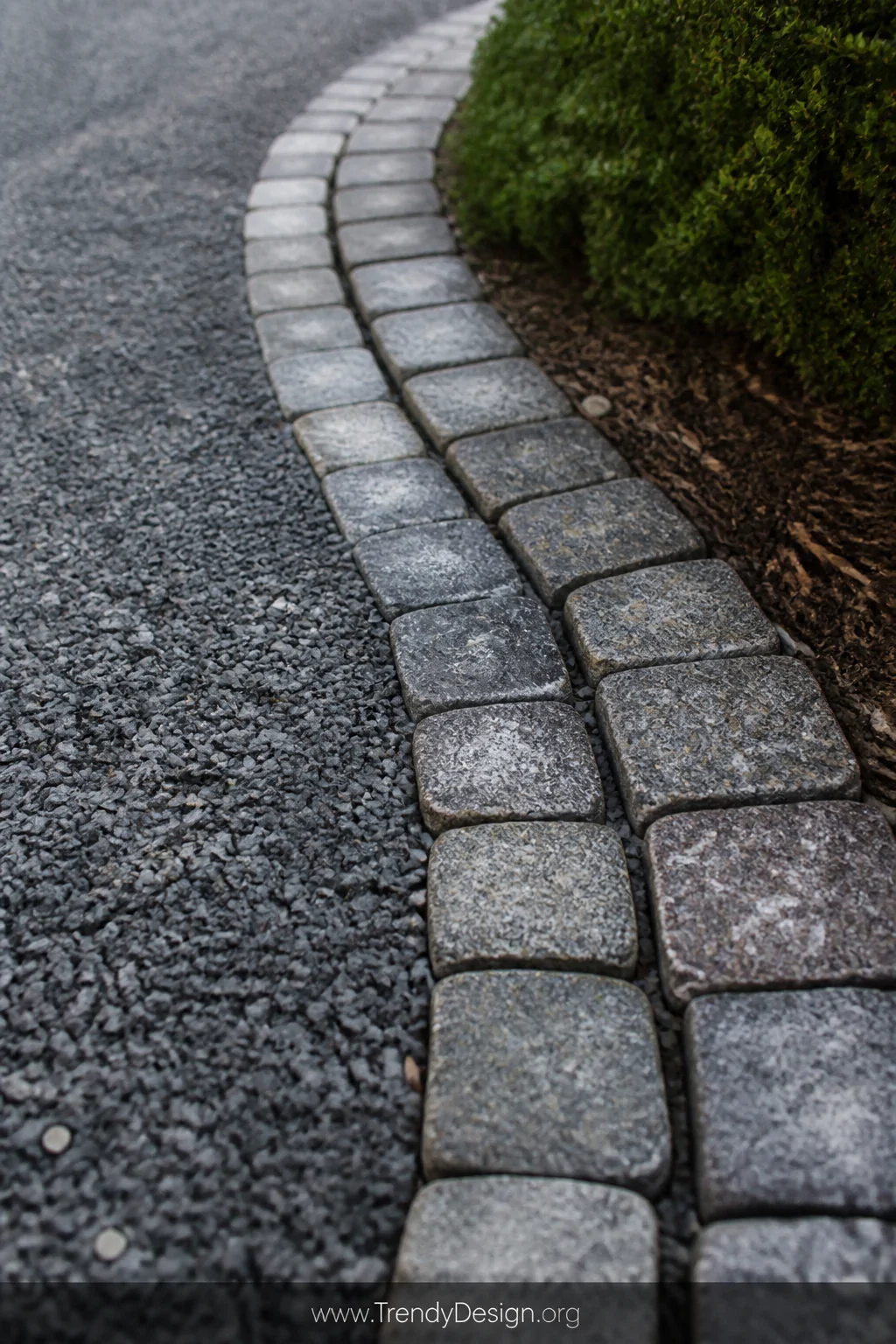 A close-up detail shot of genuine dark grey granite sett cobblestones set in a tight curved pattern along the edge of a grave